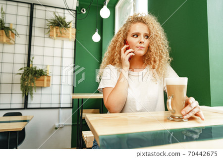 Young beautiful woman talking on the phone in cafeteria Young beautiful woman talking on the phone in cafeteria 70442675