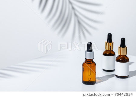 Creative photo of cosmetic bottle with pipette on a white background with shadow of tropical flower Creative photo of cosmetic bottle with pipette on a white background with shadow of tropical flower 70442834