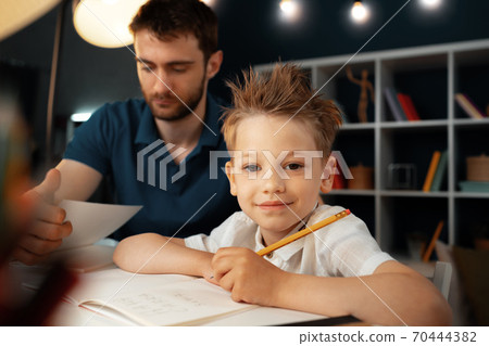 Dad and son doing school homework together Dad and son doing school homework together 70444382