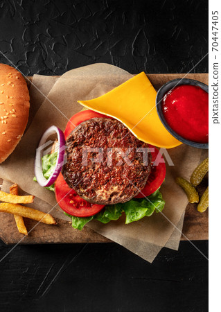 Burger with beef, cheese, onion, tomato, and green salad, with a bun and ketchup, with French fries, overhead shot with a place for text Burger with beef, cheese, onion, tomato, and green salad, with a bun and ketchup, with French fries, overhead shot with a place for text 70447405