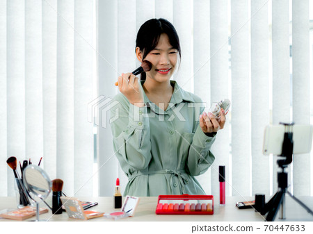 Beautiful Asia female vlogger is showing cosmetics makeup products while recording video and giving recommended for her beauty blog with digital smartphone Beautiful Asia female vlogger is showing cosmetics makeup products while recording video and giving recommended for her beauty blog with digital smartphone 70447633