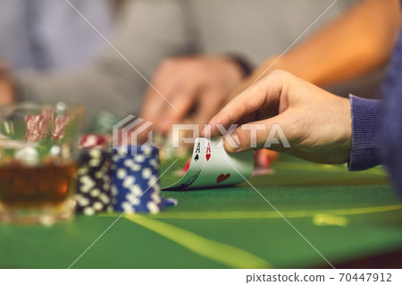 Closeup of gambler's hand holding a pair of aces while playing poker on casino night Closeup of gambler's hand holding a pair of aces while playing poker on casino night 70447912