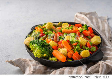 Mixture of frozen vegetables corn, red pepper, peas, carrots, broccoli, tomatoes in a cast-iron 70449114