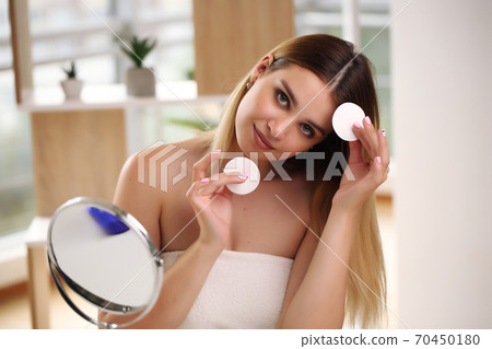 Girl in the bathroom, cleansing the skin with a cotton pad, taking care of the condition of his face, enjoying the rituals of beauty in the morning Girl in the bathroom, cleansing the skin with a cotton pad, taking care of the condition of his face, enjoying the rituals of beauty in the morning 70450180