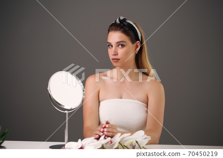 Young attractive girl with white hair, big eyes, thick eyebrows and bare shoulders holding hand near face on gray background, portrait, copy space. Young attractive girl with white hair, big eyes, thick eyebrows and bare shoulders holding hand near face on gray background, portrait, copy space. 70450219