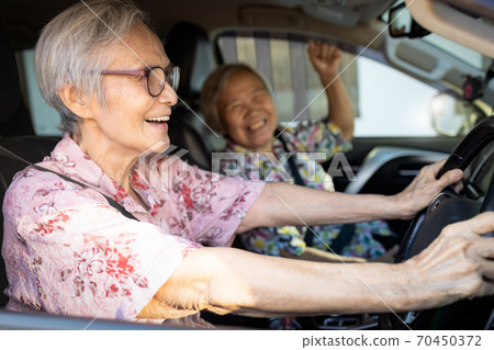 Happy asian senior female driver in her car,enjoy traveling during retirement age with her friend,healthy old people having fun,laughing together,elderly woman driving car,road trip,travel concept 70450372