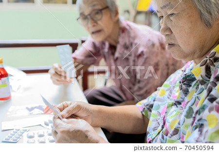 Asian female senior hold medicine pill in hand,elderly woman consult her old people friend,help and read medicine labels drug prescription,discussing medication, directions of use,side effects Asian female senior hold medicine pill in hand,elderly woman consult her old people friend,help and read medicine labels drug prescription,discussing medication, directions of use,side effects 70450594
