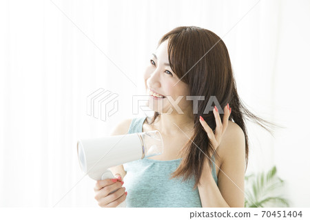 A woman drying her hair with a dryer. 70451404