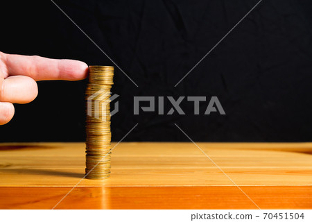Finger pushing a column of coins on wooden table with black wall, gold coins falls , business crisis concept. shallow focus Finger pushing a column of coins on wooden table with black wall, gold coins falls , business crisis concept. shallow focus 70451504