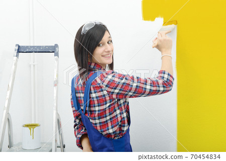 pretty young woman paints the wall yellow color 70454834