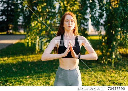 Portrait of attractive meditative young woman with closed eyes performing making hand namaste 70457590