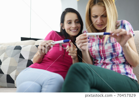 Two women are sitting on couch and looking at pregnancy tes Two women are sitting on couch and looking at pregnancy tes 70457829