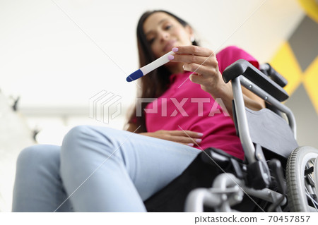 Woman in wheelchair is sitting and looking at pregnancy test Woman in wheelchair is sitting and looking at pregnancy test 70457857