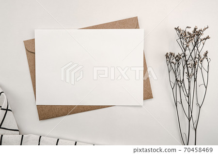 Blank white paper on brown paper envelope with Limonium dry flower and White cloth with Black grid pattern. Mock-up of horizontal blank greeting card. Top view of Craft envelope on white background. 70458469
