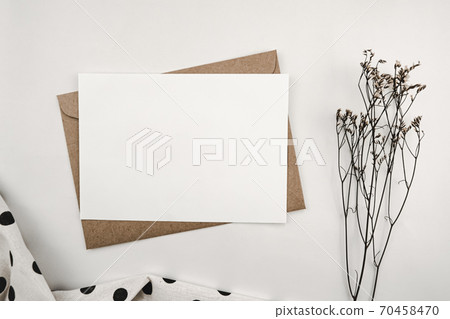 Blank white paper on brown paper envelope with Limonium dry flower and White cloth with black dots. Mock-up of horizontal blank greeting card. Top view of Craft envelope on white background. 70458470