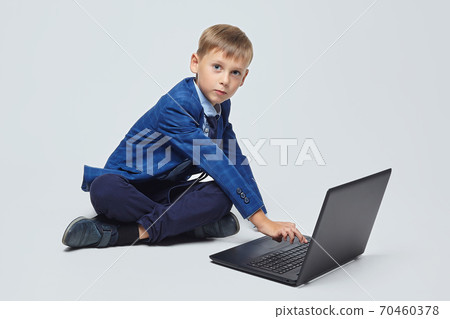 attractive blond boy in school suit sits in front of open laptop attractive blond boy in school suit sits in front of open laptop 70460378