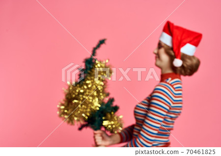 Woman with a Christmas tree in her hands and yellow shiro red cap pink background 70461825