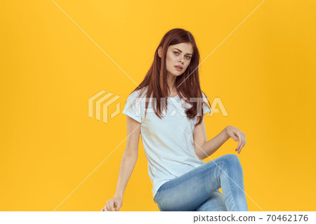 Woman sitting on a chair white t-shirt jeans fashionable clothes glamor studio yellow background Woman sitting on a chair white t-shirt jeans fashionable clothes glamor studio yellow background 70462176