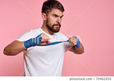Sporty man in a white T-shirt boxing bandages on the hands of a workout lifestyle pink background Sporty man in a white T-shirt boxing bandages on the hands of a workout lifestyle pink background 70462850