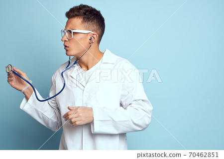A medical worker in a dressing gown and glasses holds a stethoscope in his hands on a blue background cropped view A medical worker in a dressing gown and glasses holds a stethoscope in his hands on a blue background cropped view 70462851