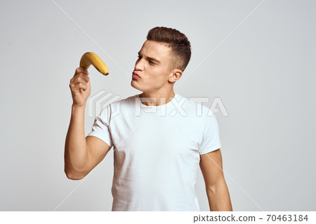 guy with a banana in his hand on a light background fun emotions light background white t-shirt model guy with a banana in his hand on a light background fun emotions light background white t-shirt model 70463184