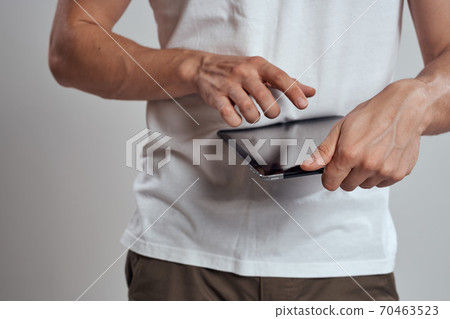 Tablet with a touch screen on a light background male hands white t-shirt cropped view Tablet with a touch screen on a light background male hands white t-shirt cropped view 70463523