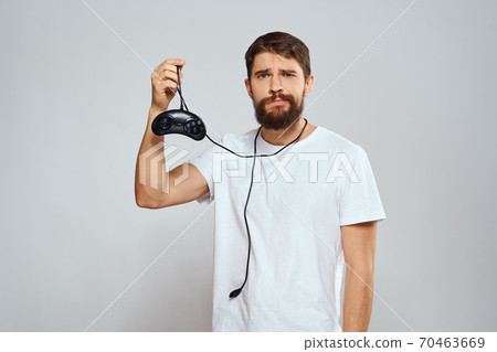 A man with a gamepad in his hands playing games leisure lifestyle technology white t-shirt light background 70463669