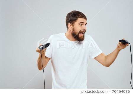A man holds in his hands two joysticks playing leisure technology lifestyle white t-shirt A man holds in his hands two joysticks playing leisure technology lifestyle white t-shirt 70464086