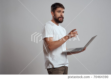 A man with a laptop in his hands on a light background in a white t-shirt emotions light background new technologies 70464390