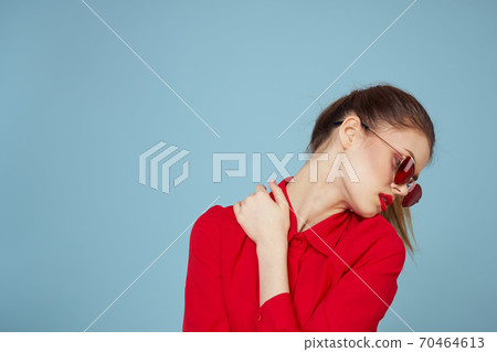 Woman in red shirt on blue background holds hands near face and sunglasses red lips makeup model Woman in red shirt on blue background holds hands near face and sunglasses red lips makeup model 70464613