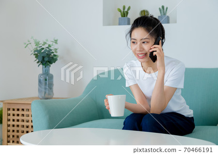 Beautiful woman drinking coffee in living room and talking on mobile phone Beautiful woman drinking coffee in living room and talking on mobile phone 70466191