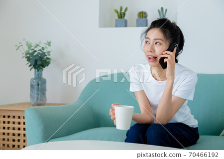Beautiful woman drinking coffee in living room and talking on mobile phone Beautiful woman drinking coffee in living room and talking on mobile phone 70466192