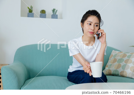 Beautiful woman drinking coffee in living room and talking on mobile phone Beautiful woman drinking coffee in living room and talking on mobile phone 70466196