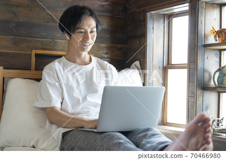 一個年輕人坐在床上,看著筆記本電腦的屏幕 一個年輕人坐在床上,看著筆記本電腦的屏幕 70466980