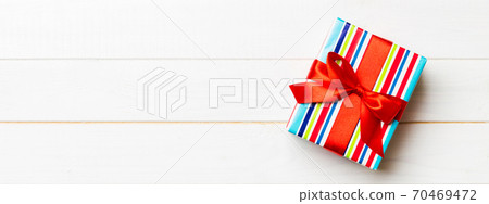 Beautiful gift box with a colored bow on the white wooden table. Top view with copy space for you design. Christmas concept Beautiful gift box with a colored bow on the white wooden table. Top view with copy space for you design. Christmas concept 70469472