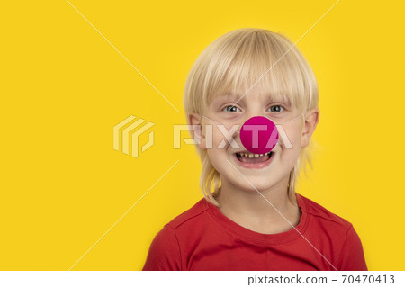 Cute blond boy wears clown nose and smiling. Portrait child close up on yellow background 70470413