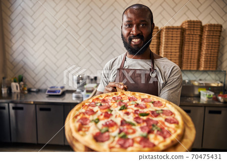 Joyful Afro American man holding wooden board with pizza 70475431