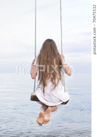 Girl in white dress swinging over the water, enjoying the sea view. Vertical frame. Back view Girl in white dress swinging over the water, enjoying the sea view. Vertical frame. Back view 70475532