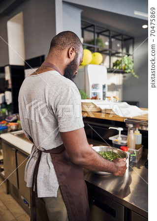 Young man washing greenery in professional kitchen Young man washing greenery in professional kitchen 70475869