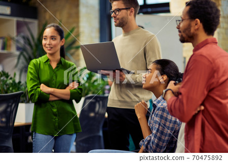 Group of young diverse multi ethnic business people using laptop and discussing project results while standing together in modern office Group of young diverse multi ethnic business people using laptop and discussing project results while standing together in modern office 70475892
