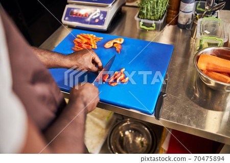 Man cutting carrot and pepper in professional kitchen Man cutting carrot and pepper in professional kitchen 70475894