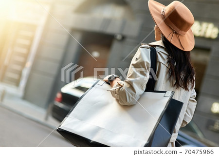 Young woman wearing hat with big shopping bag walking city streets 70475966