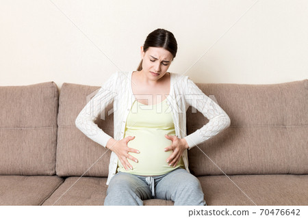 Pregnant woman with painful belly on sofa at home Pregnant woman with painful belly on sofa at home 70476642