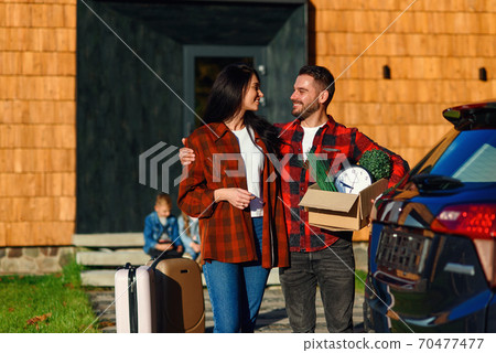 Adorable couple in love looking to each other standing near modern house with carton box during moving to the new house. Adorable couple in love looking to each other standing near modern house with carton box during moving to the new house. 70477477