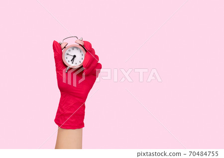 Female hand in a rubber glove holding alarm clock on pink background Female hand in a rubber glove holding alarm clock on pink background 70484755