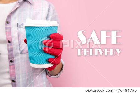 Female hand in a rubber glove holding blue paper cup on pink background Female hand in a rubber glove holding blue paper cup on pink background 70484759