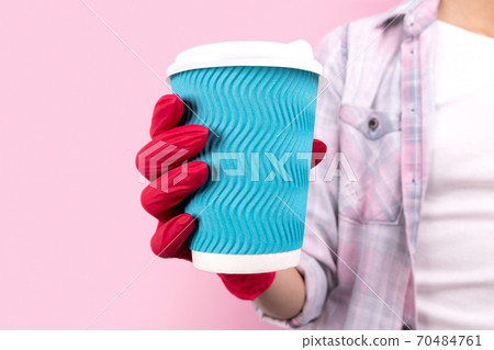 Female hand in a rubber glove holding blue paper cup on pink background Female hand in a rubber glove holding blue paper cup on pink background 70484761