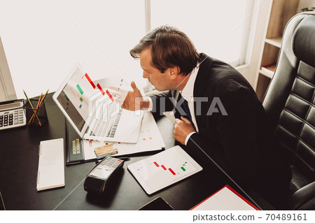 Businessman concentrate and look stress with bad result on laptop  with visual graphic that showing company profit lost in office desk atmosphere next to the window, concept worry for business crisis. 70489161
