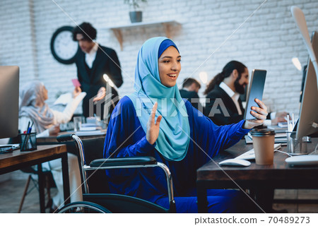 Woman in hijab sits and greets someone in computer 70489273