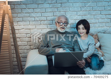 Grandfather and grandson are sitting watching movie at night at home. 70489275